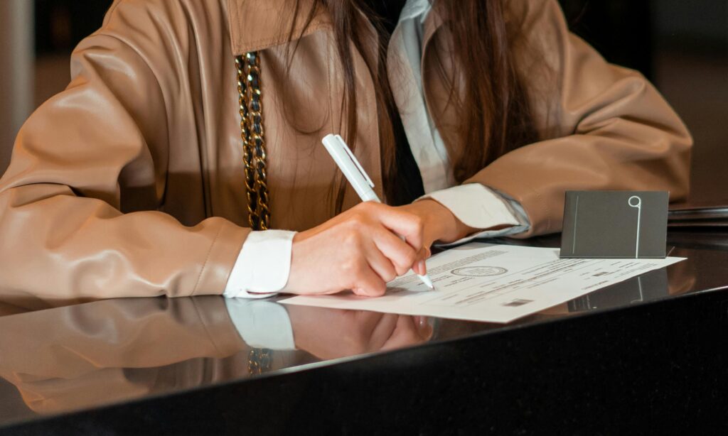 pexels-photo-7820383-7820383 Close-up of a woman signing a document at a sleek reception counter, indoor setting.